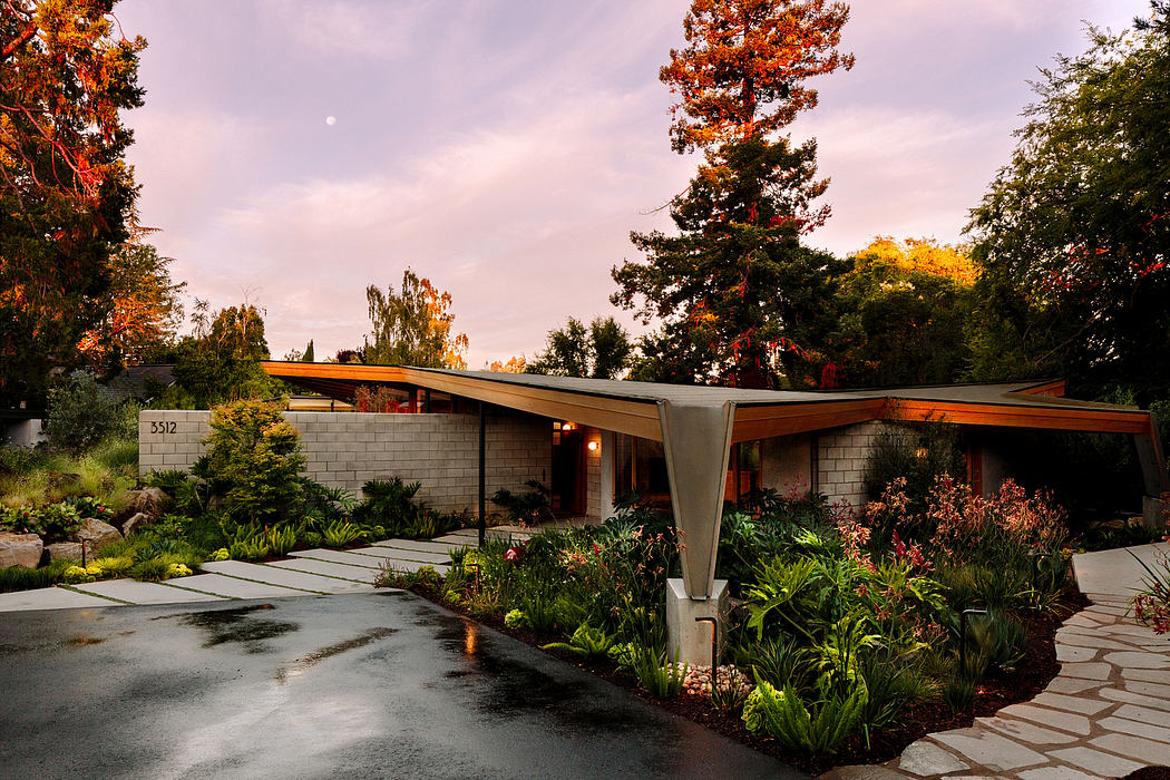 A mid-century modern home with a mix of wooden and concrete elements, surrounded by lush foliage.