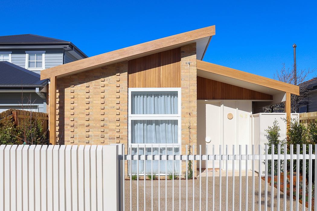 A modern building with a wooden roof, brick walls, and a white picket fence surrounding it.