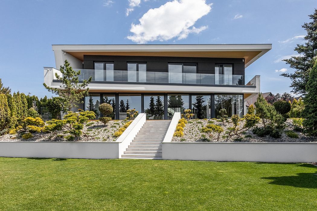 Modern two-story residential building with sleek glass facade, surrounded by lush landscaping.