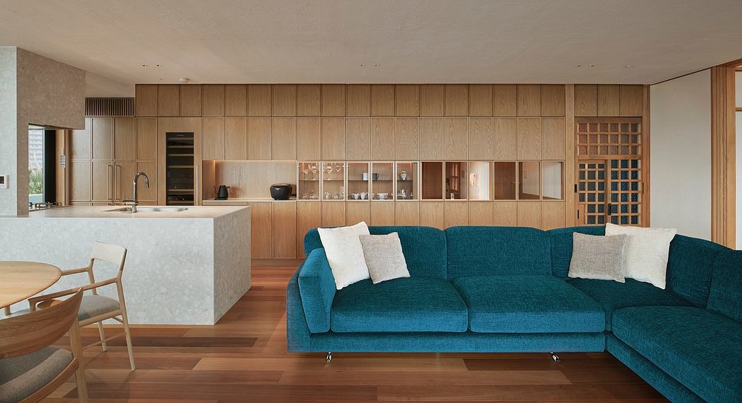 Warm, modern living room with wooden paneled walls, teal sectional, and open kitchen.