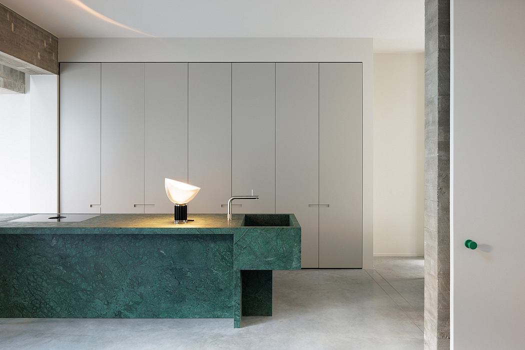 Modern kitchen featuring sleek gray cabinets, green marble countertop, and sculptural lighting.