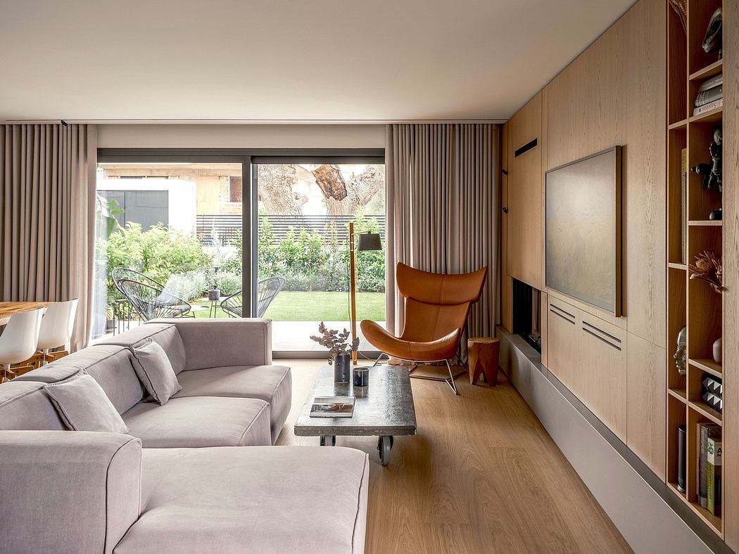 Warm, minimalist living room with large windows, grey sectional, and leather armchair.