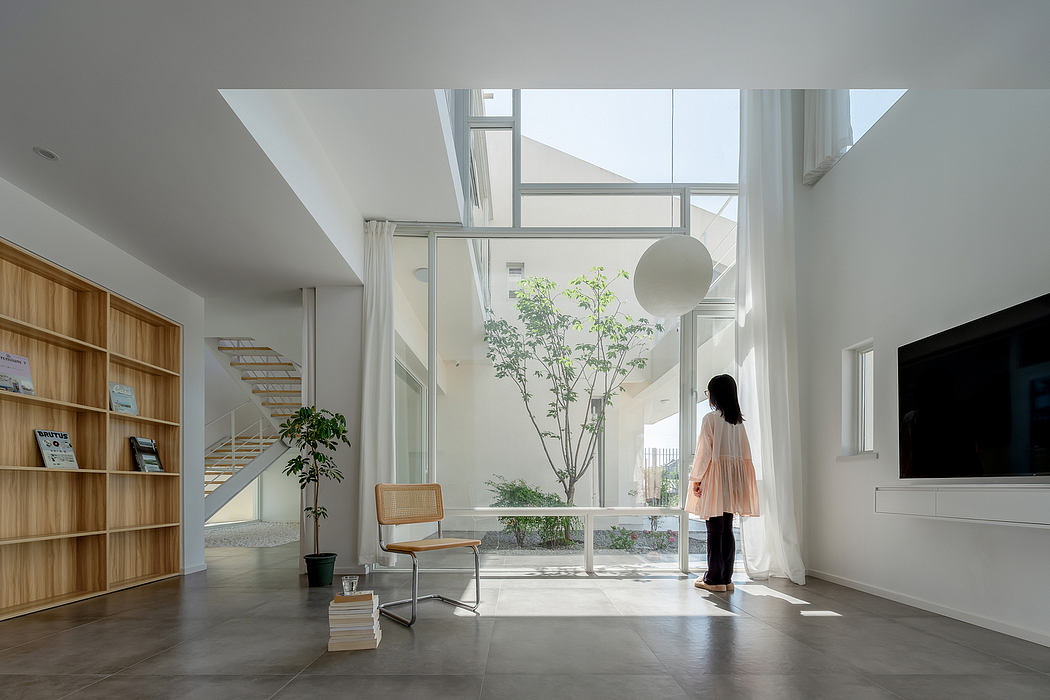 A bright, modern interior with minimalist furniture, a central plant, and views to the outdoors.