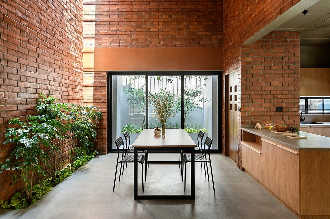 Minimalist dining area with exposed brick walls, wooden table, and black chairs surrounded by greenery.