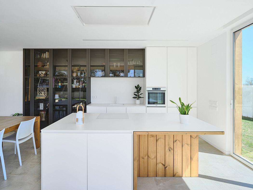 A modern, minimalist kitchen with sleek white cabinetry, wooden accents, and a large window.