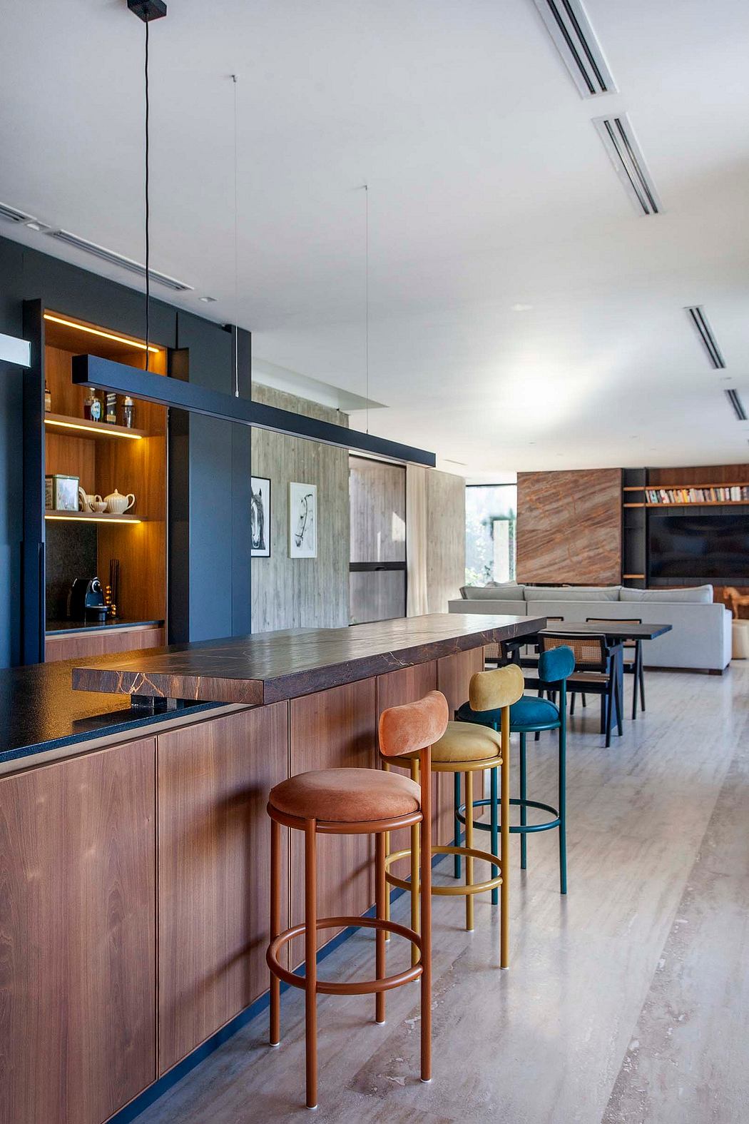 A modern open-concept kitchen with a wooden bar counter, artistic shelving, and colorful stools.
