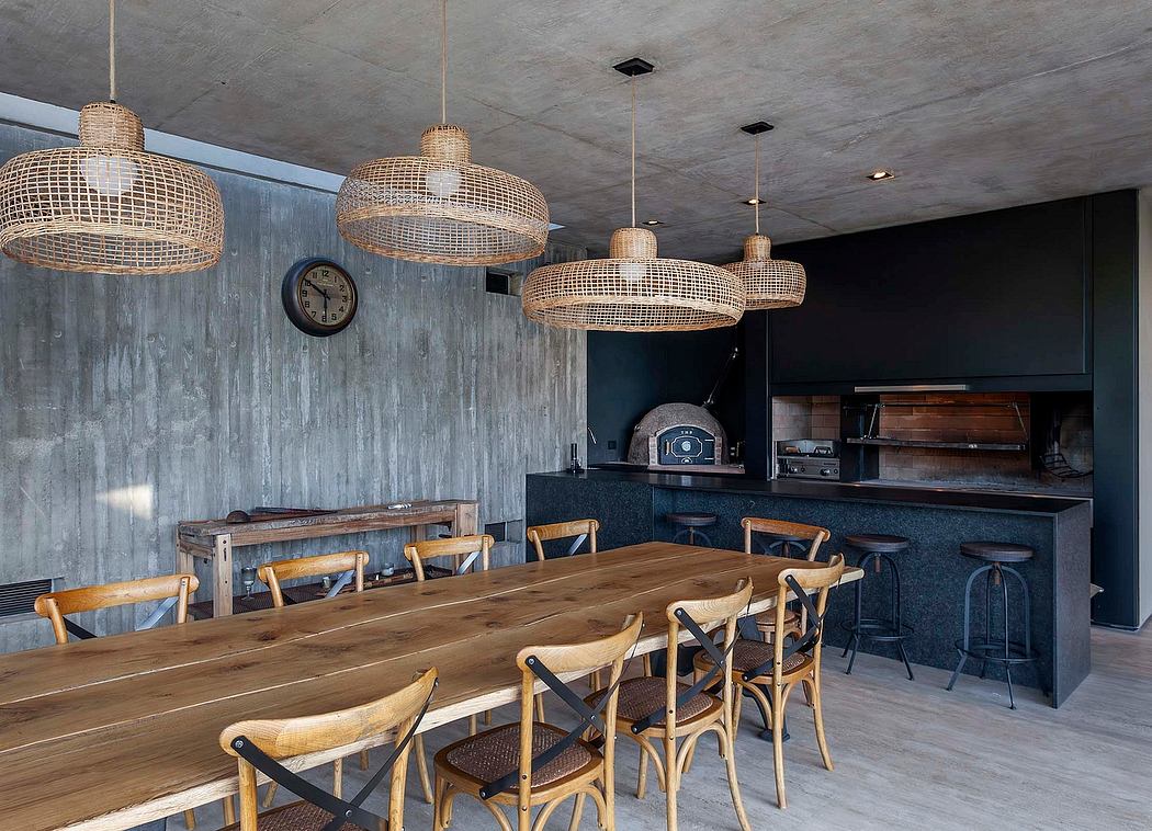 A modern industrial-style dining area with a large wooden table, woven pendant lights, and a built-in kitchen.