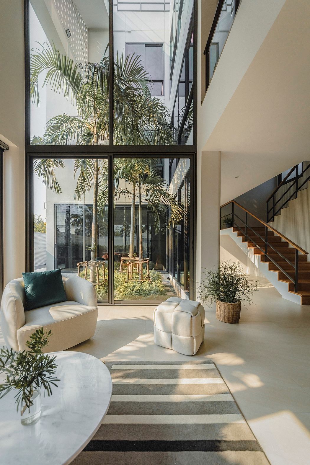 Spacious modern living room with tall glass walls, lush palm trees, and minimalist furniture.