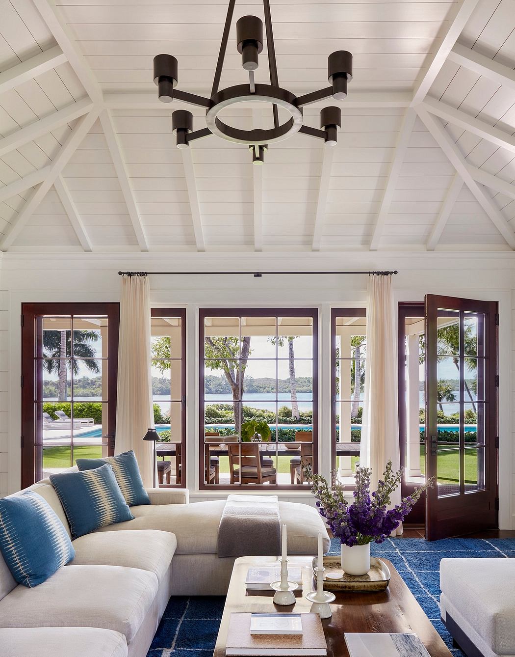 Spacious living room with high-ceiched vaulted ceiling, large windows offering scenic views, and a modern chandelier.