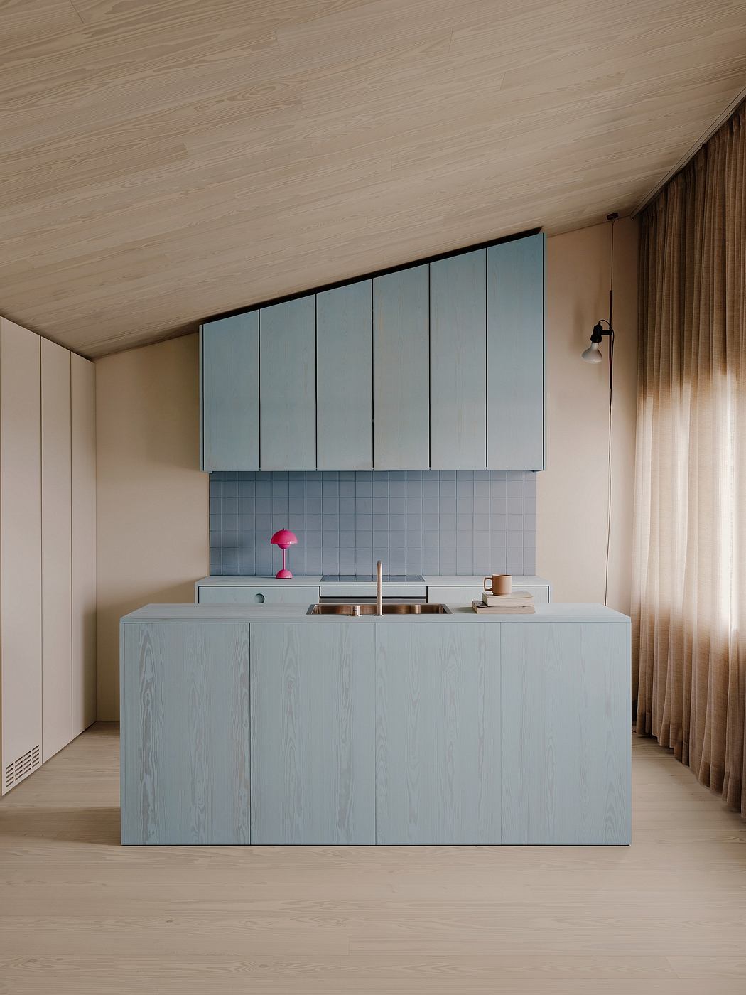 A modern kitchen with a sleek, minimalist blue island and storage cabinets against a light wood backdrop.