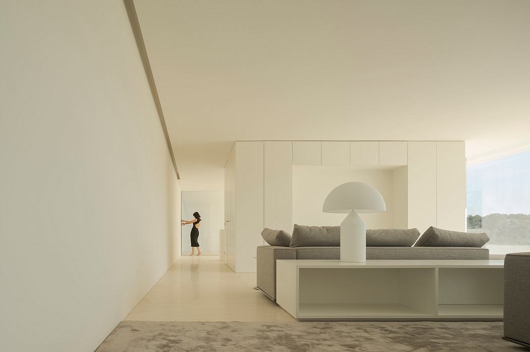 Modern, minimalist living room with clean lines, built-in furniture, and a glimpse of a person in the distance.