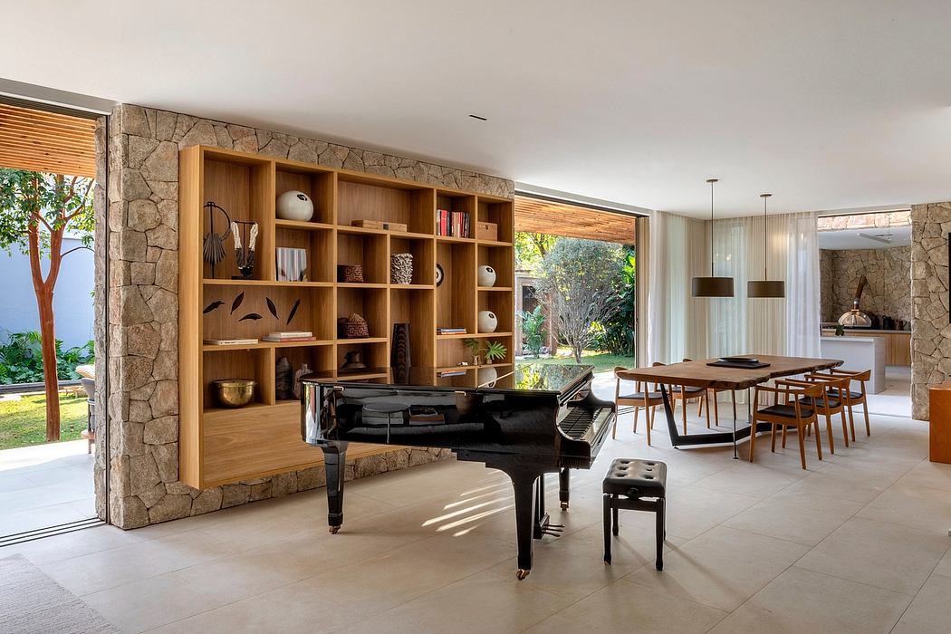 Spacious open-plan room with stone walls, wooden shelving, and a grand piano. Sliding glass doors lead to a garden.