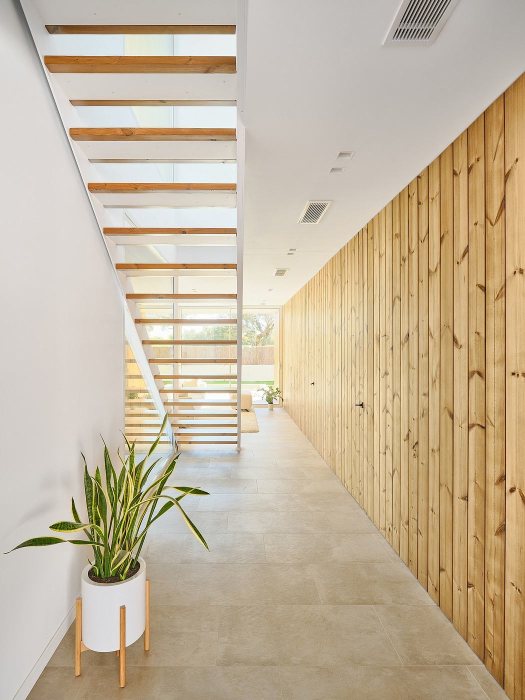 A bright, minimalist hallway with wooden paneling and a glass-and-wood staircase.