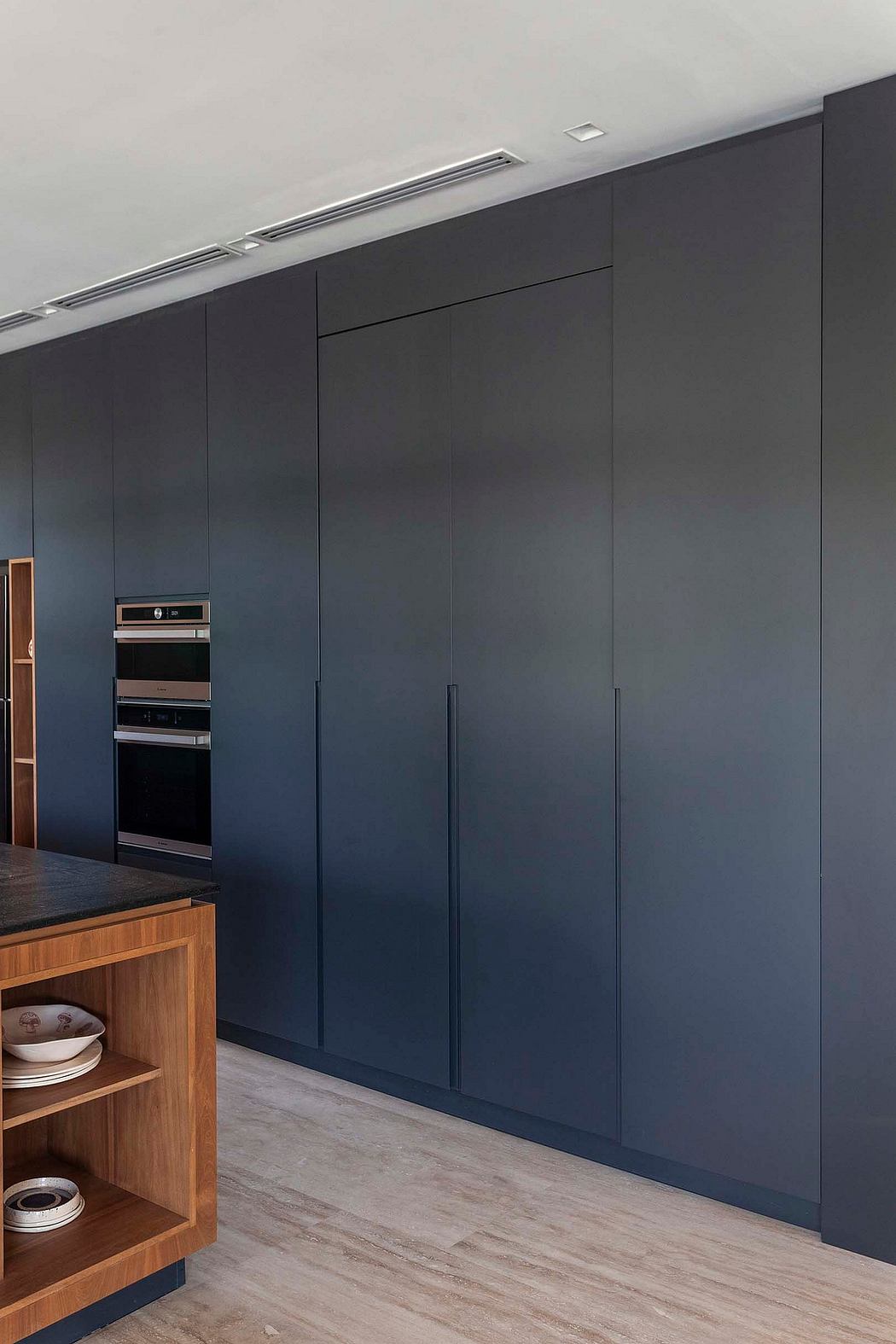 The image depicts a minimalist, modern kitchen with sleek black cabinetry, built-in appliances, and wooden accents.