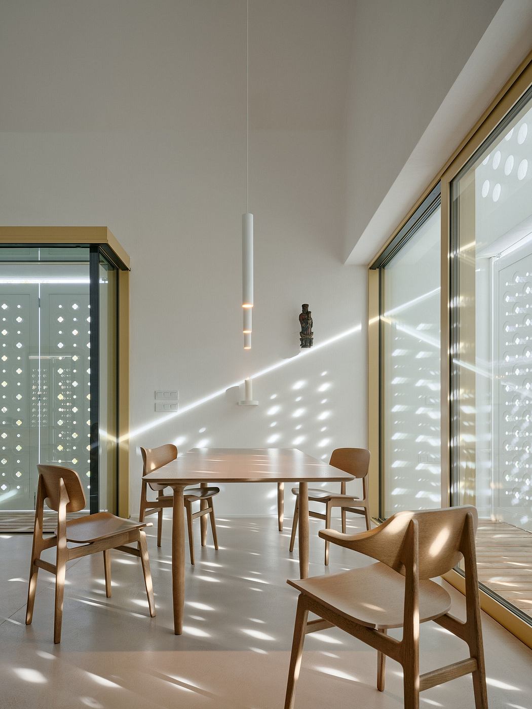 A modern, minimalist dining area with wooden furniture and natural lighting from floor-to-ceiling windows.