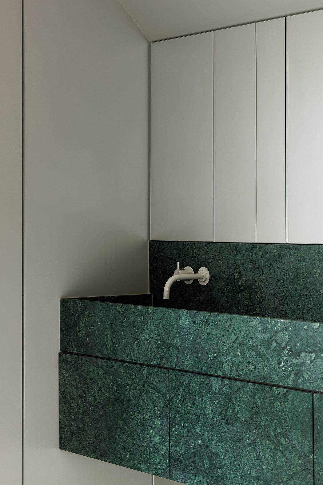 A minimalist vanity with a dark green marble countertop and recessed white fixtures.