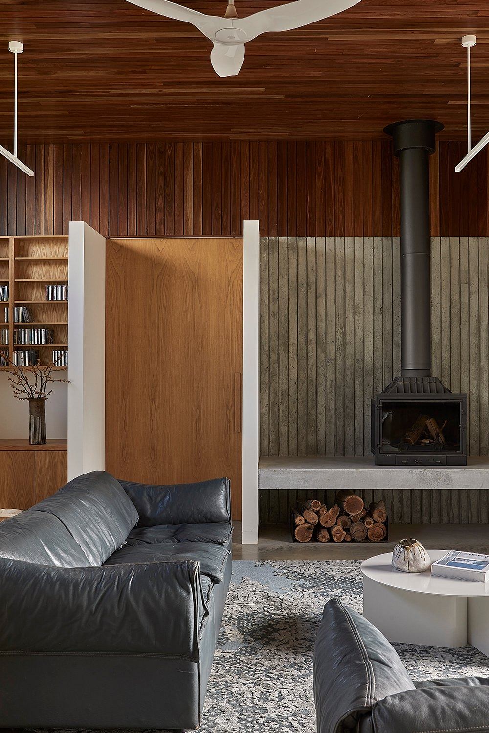 A cozy, rustic living space with wood-paneled walls, a leather sofa, and a modern fireplace.