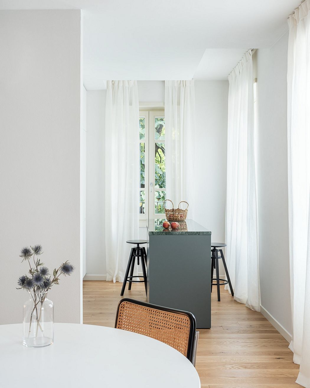 Bright, minimalist interior with white curtains, wood floors, and a gray kitchen island.