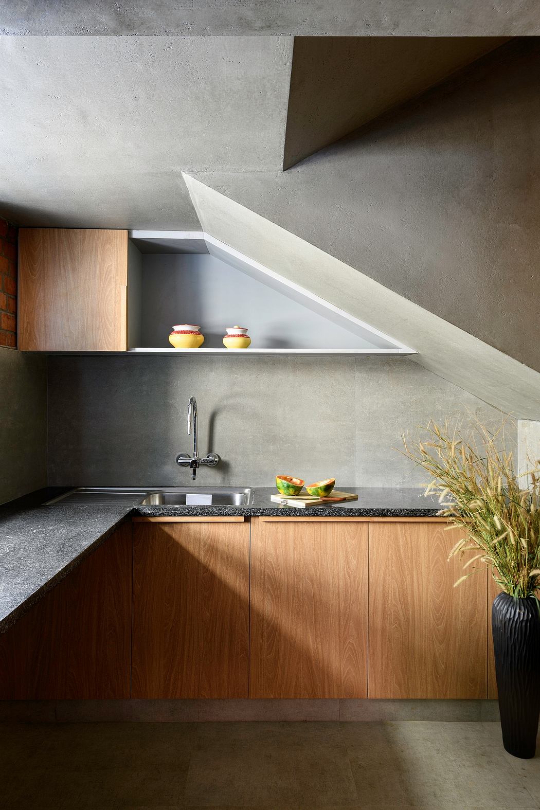 A modern kitchen interior with wooden cabinets, concrete walls, and built-in shelving.