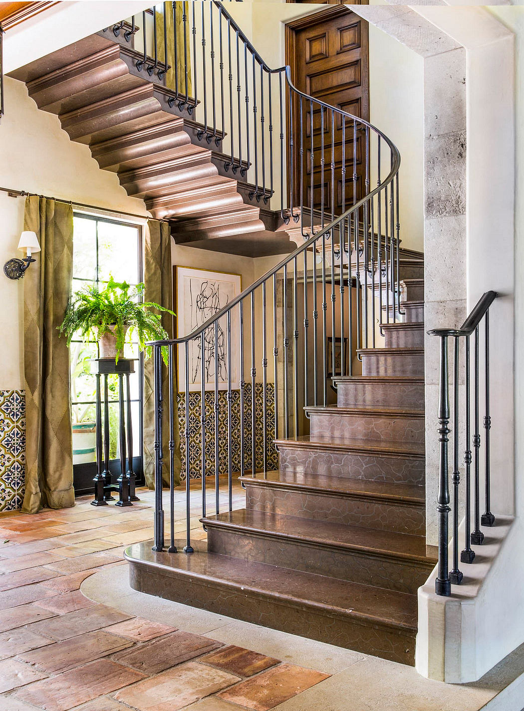 A grand entryway with spiral stairs, intricate wrought-iron railings, and rustic stone flooring.
