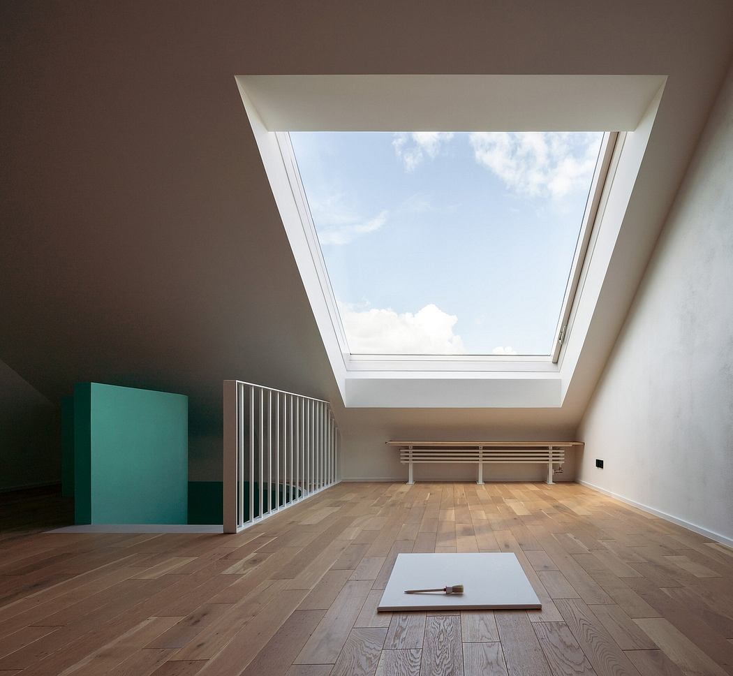 A minimalist attic space with a large skylight, wooden floors, and a modern staircase railing.