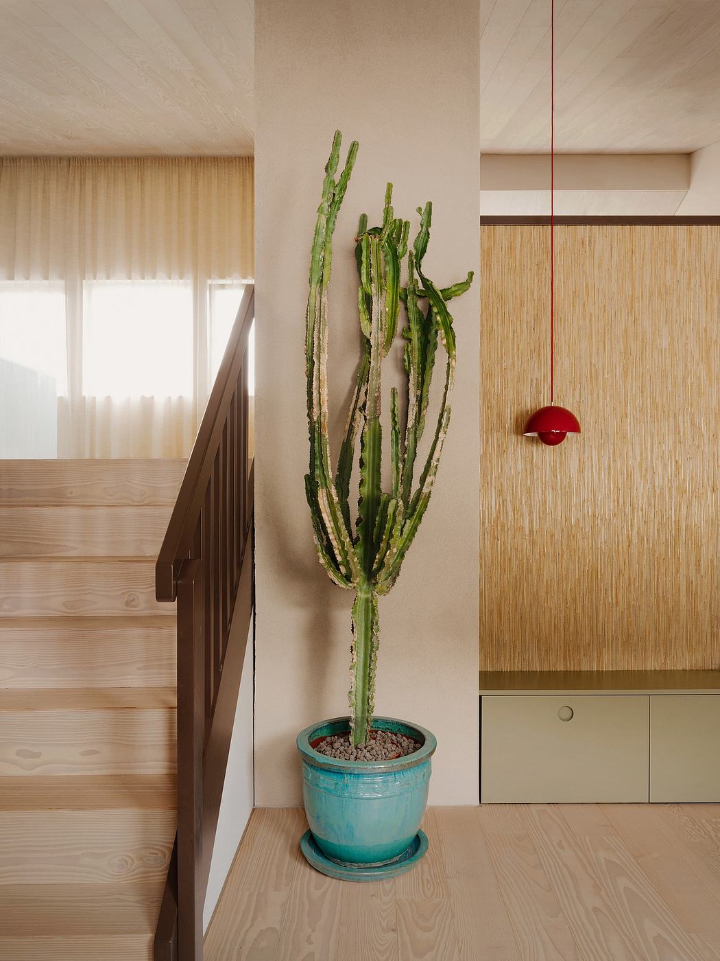 Minimalist interior with wooden floors, cactus plant, and red pendant light.