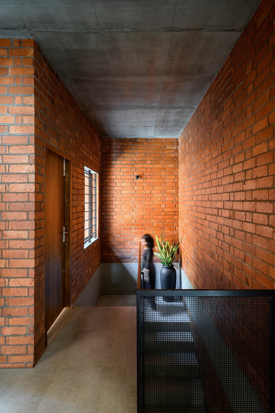 An interior view featuring exposed brick walls, a concrete ceiling, and a metal mesh staircase.