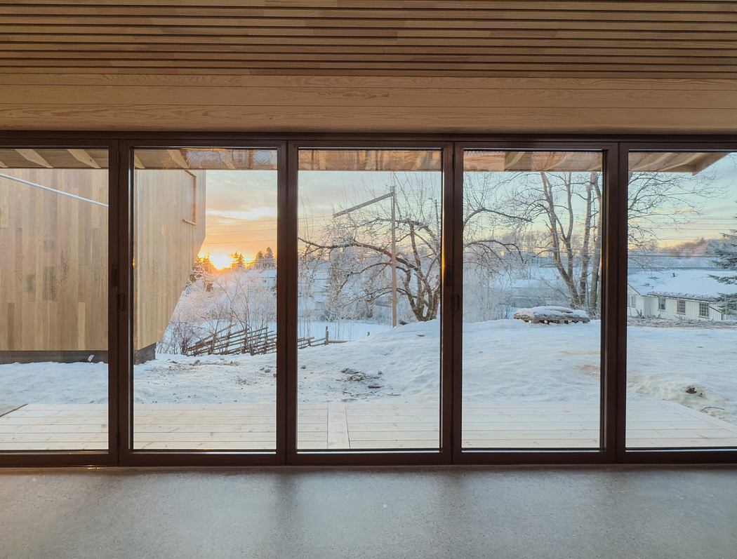 A cozy interior with large windows showcasing a snowy winter landscape at sunset.