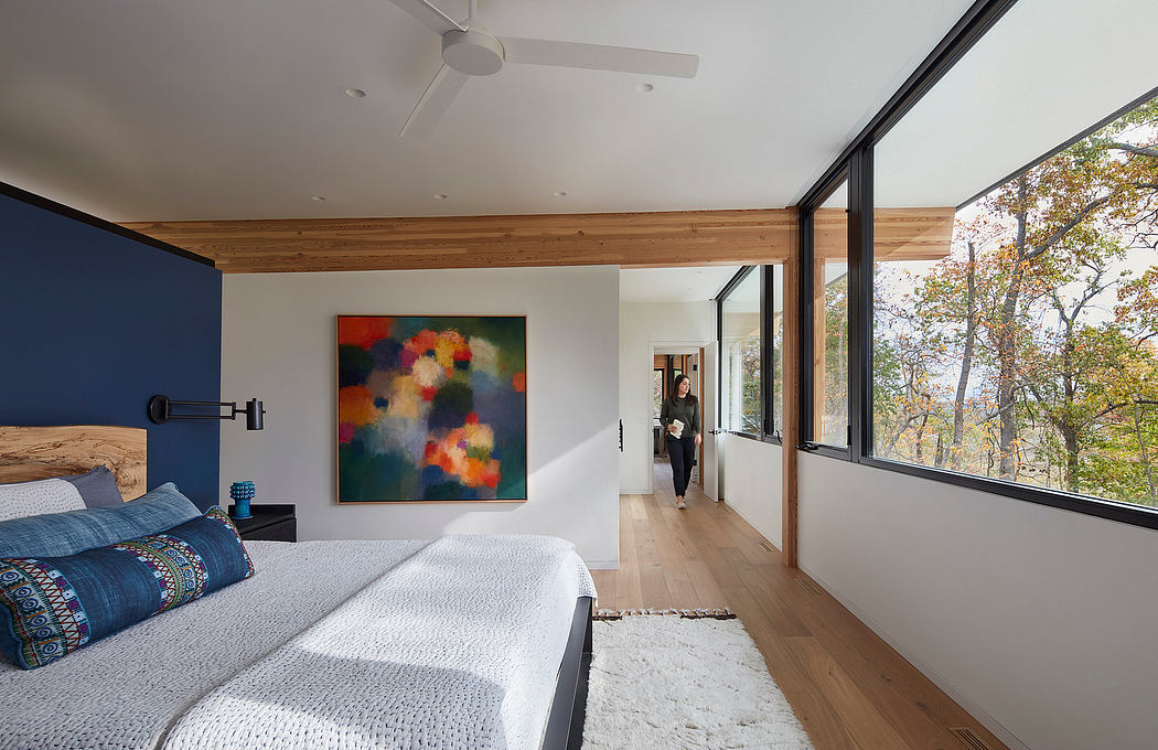Modern, spacious bedroom with wooden beams, large windows, and colorful artwork.
