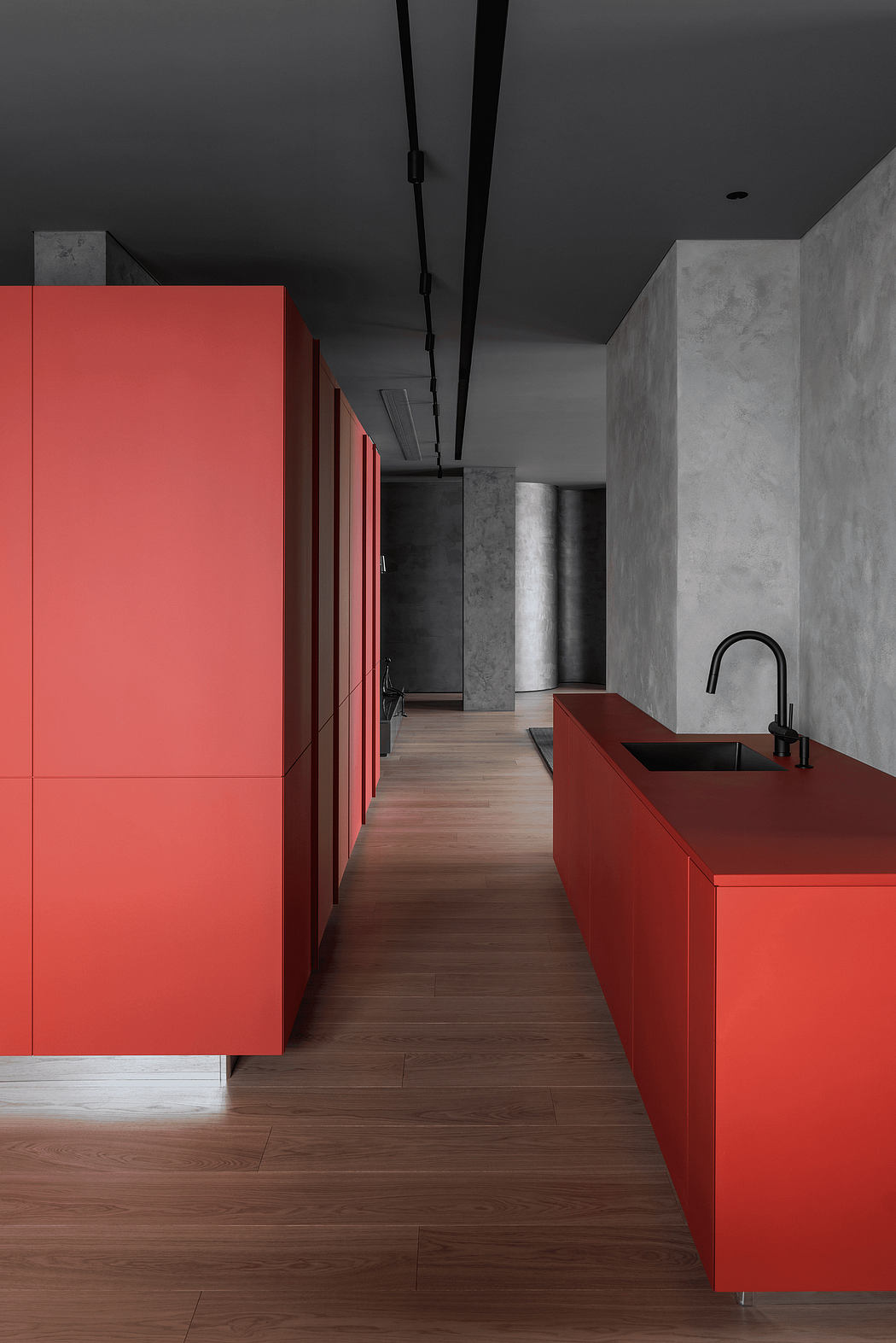 Modern, minimalist kitchen design with striking red cabinets, concrete walls, and wood floors.