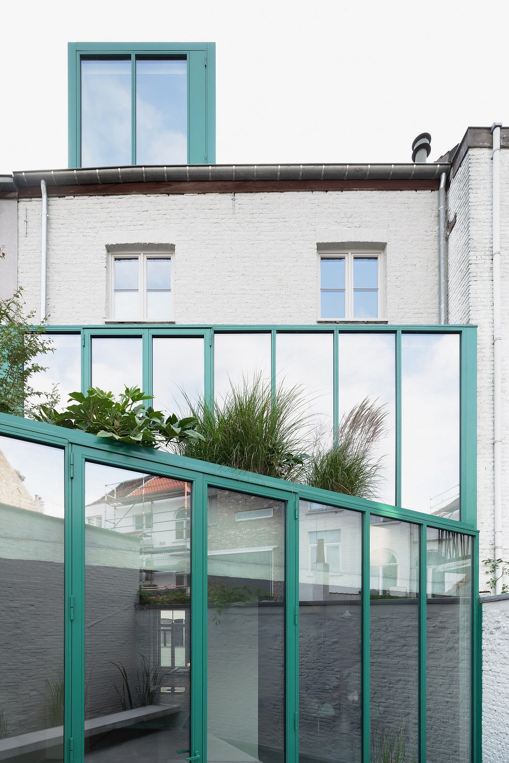 Striking minimalist facade with lush greenery atop, contrasting with the white brick walls.