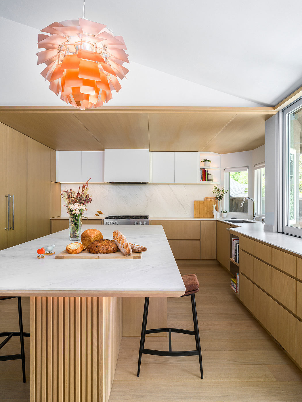 A modern kitchen with a large island, warm wood tones, and a striking pink light fixture.