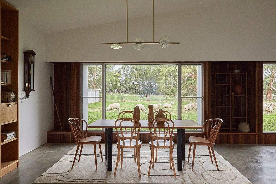 A cozy dining room with a wooden table, chairs, and a large window overlooking a pastoral scene.