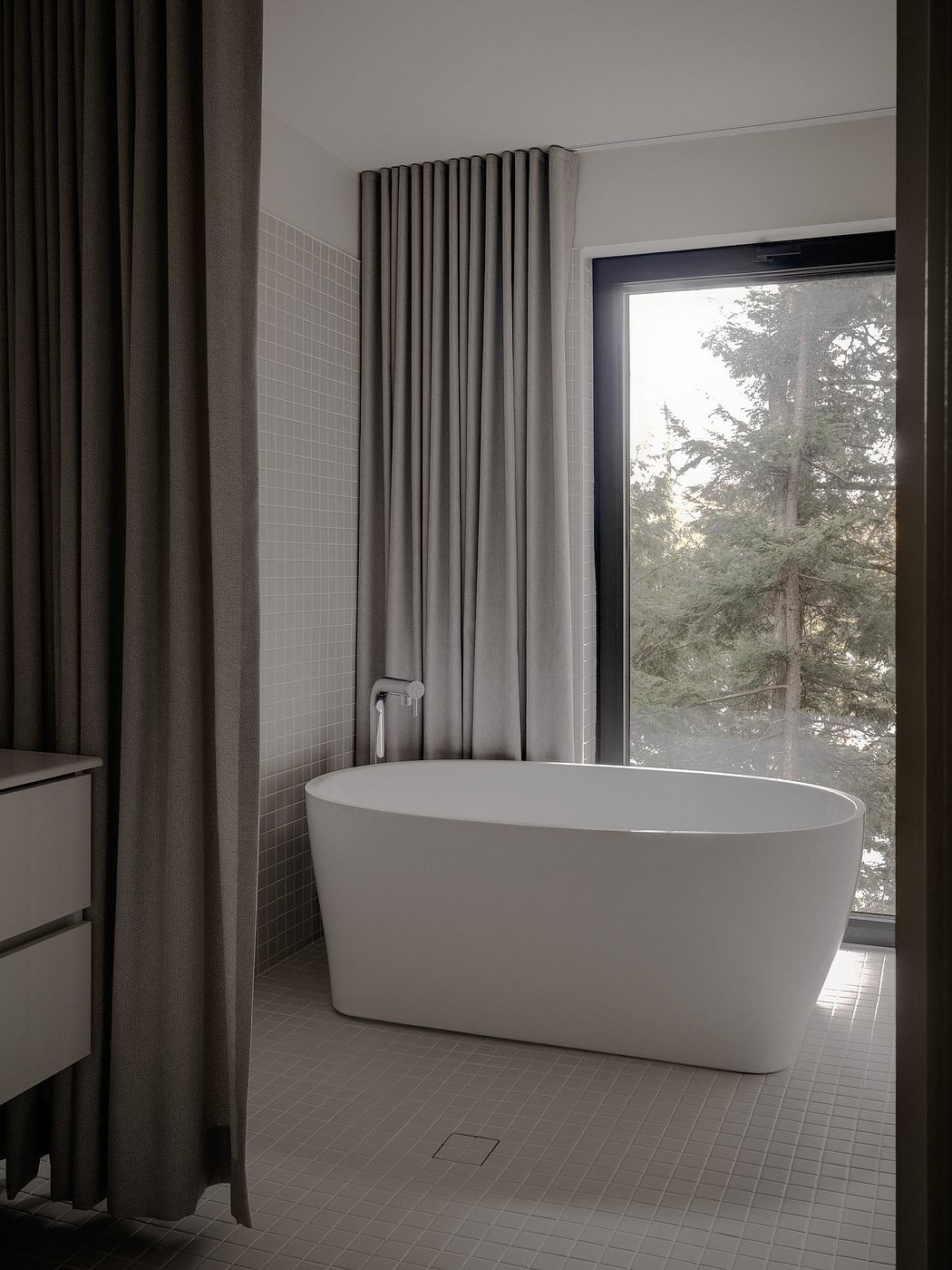 Elegant, minimalist bathroom with freestanding tub, curtains, and forest view.