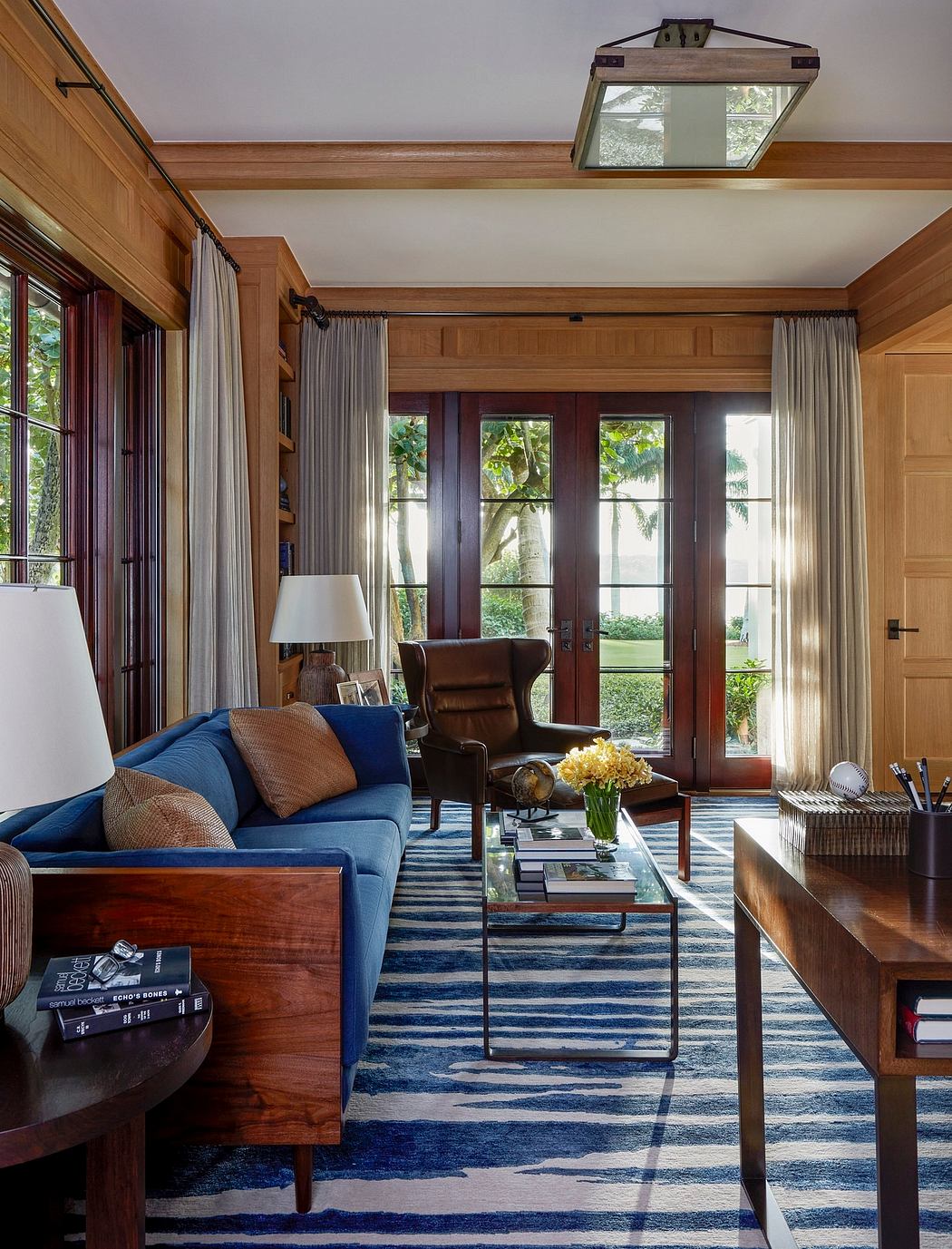 Cozy living room with warm wood paneling, large windows, and a striking blue-patterned rug.