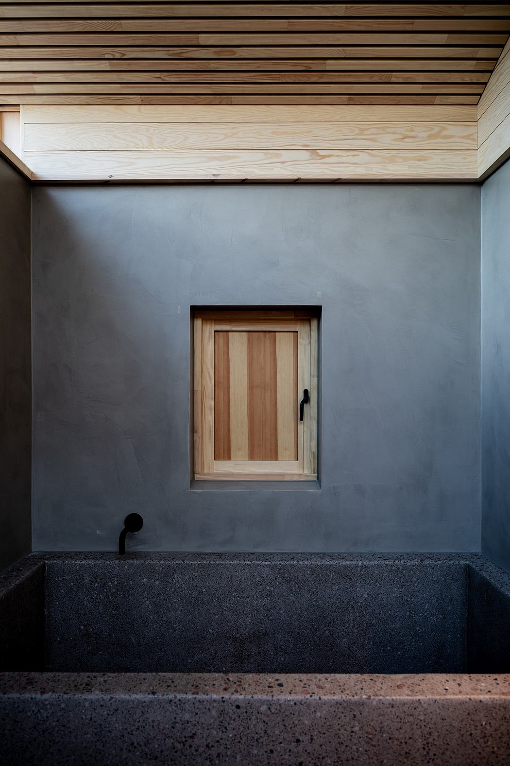 A minimalist architectural design featuring a wooden door, concrete walls, and a dark granite bench.