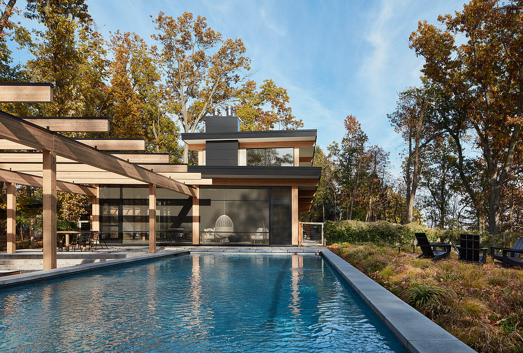 A modern, wood-and-glass home with a covered patio and an inground swimming pool surrounded by trees.