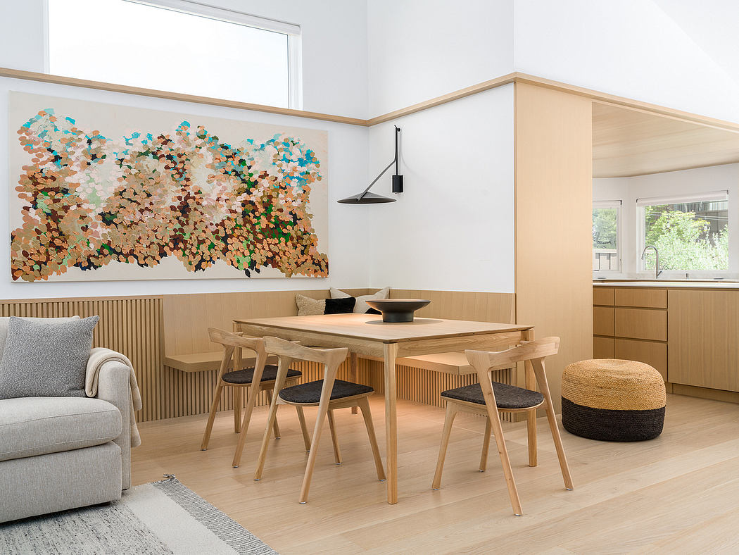 Bright, minimalist open-plan room with wooden dining table, abstract wall art, and cozy seating.