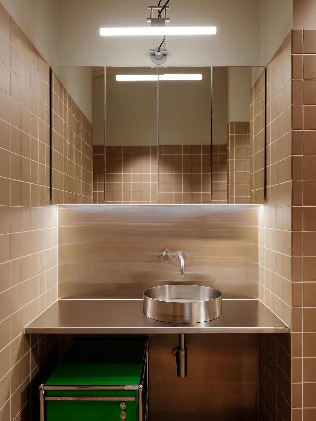 A modern bathroom with sleek lighting, a stainless steel sink, and tiled walls.