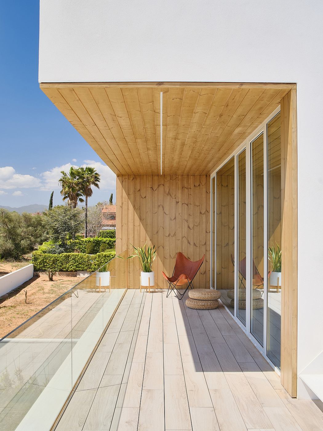 A modern wooden porch with sleek glass walls, overlooking a lush garden landscape.