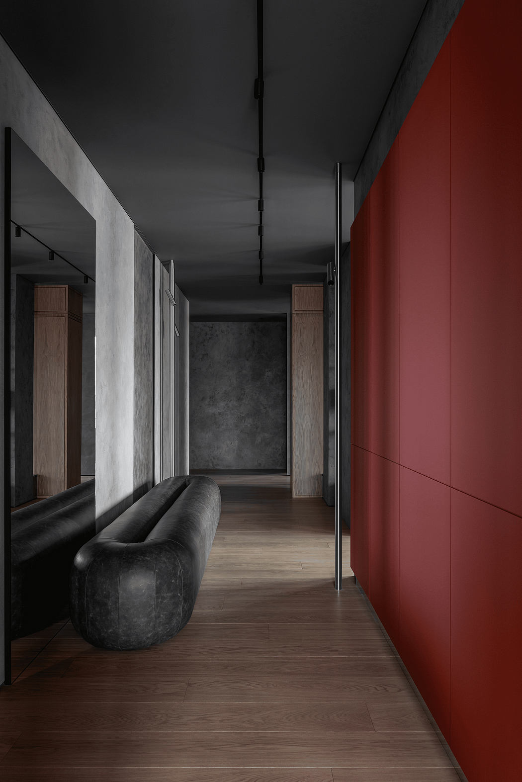 A dimly lit hallway with a bold red wall, wooden flooring, and a black leather sofa.