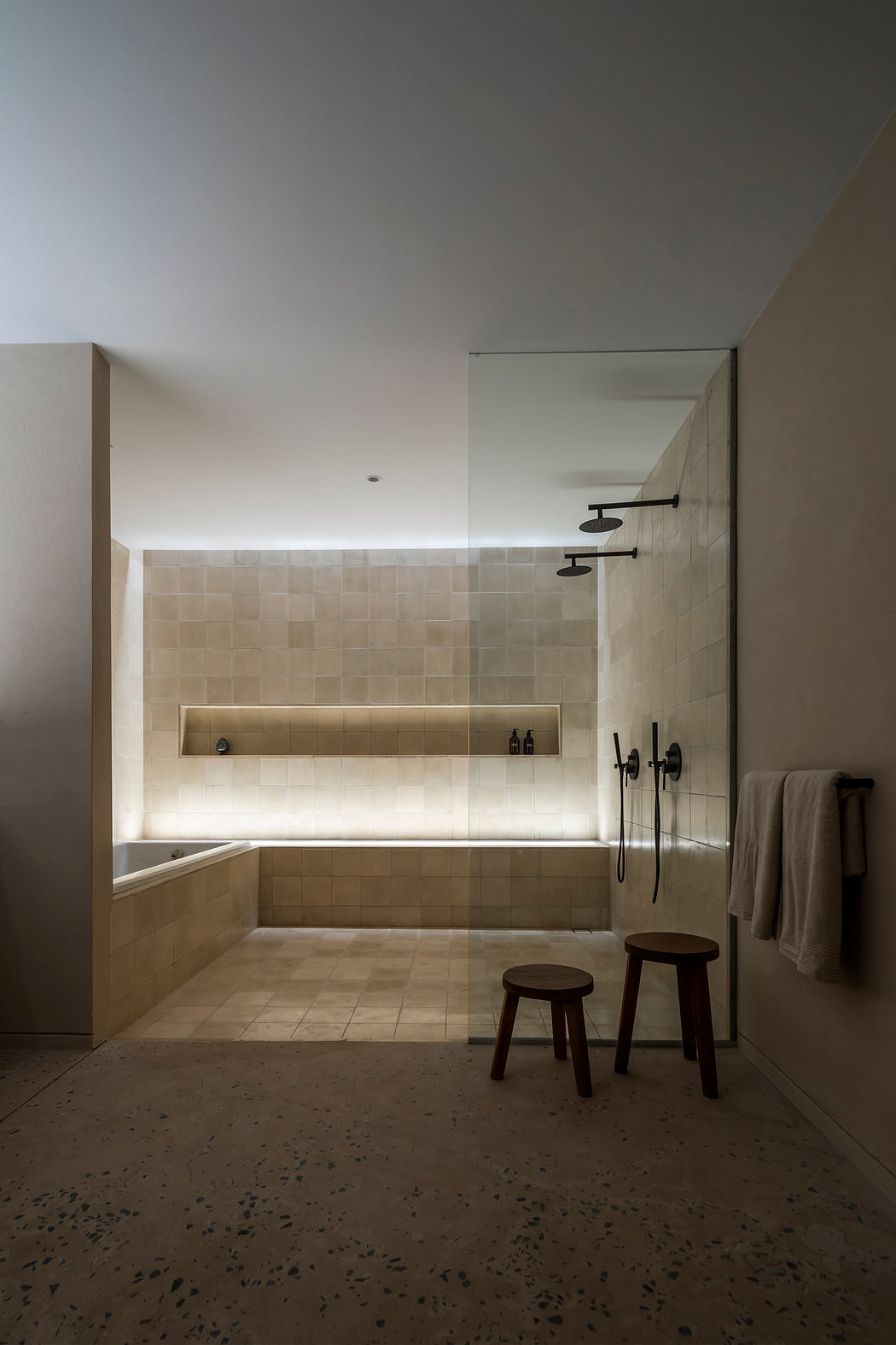 Minimalist bathroom design with recessed lighting, tiled walls, and wooden stools.