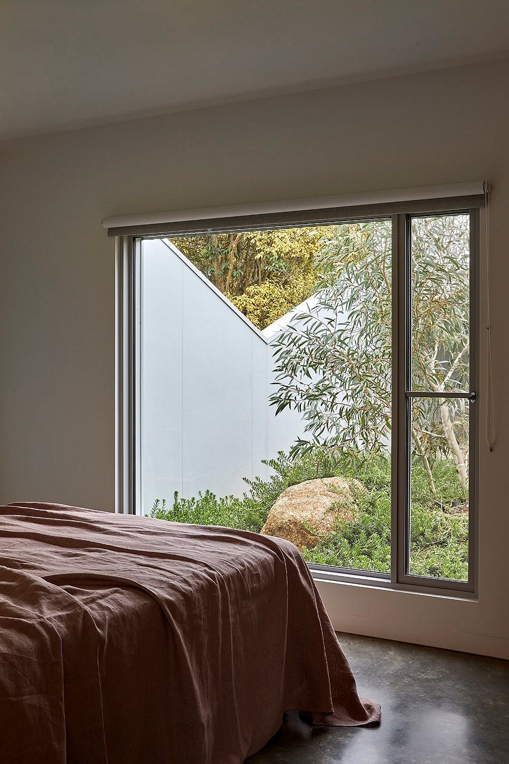 A cozy bedroom with large windows overlooking a lush, natural landscape.