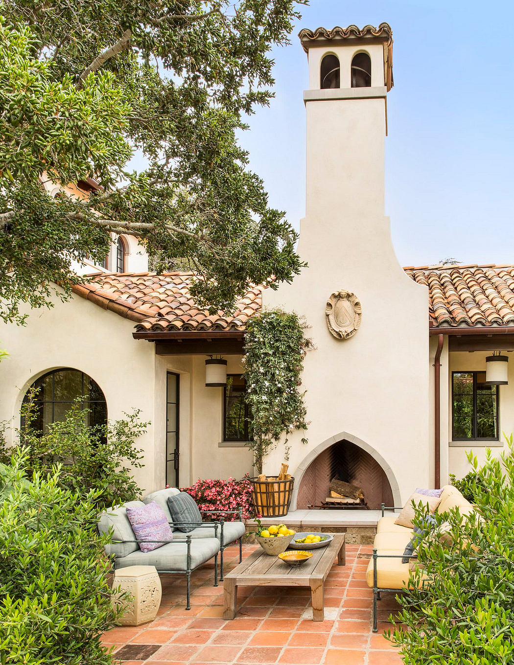 Charming Spanish-style courtyard with arched fireplace, cozy seating, and lush greenery.