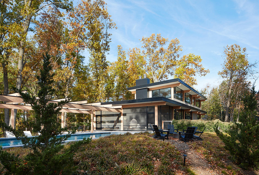 A modern, glass-walled home surrounded by lush, autumnal foliage and an inviting pool.