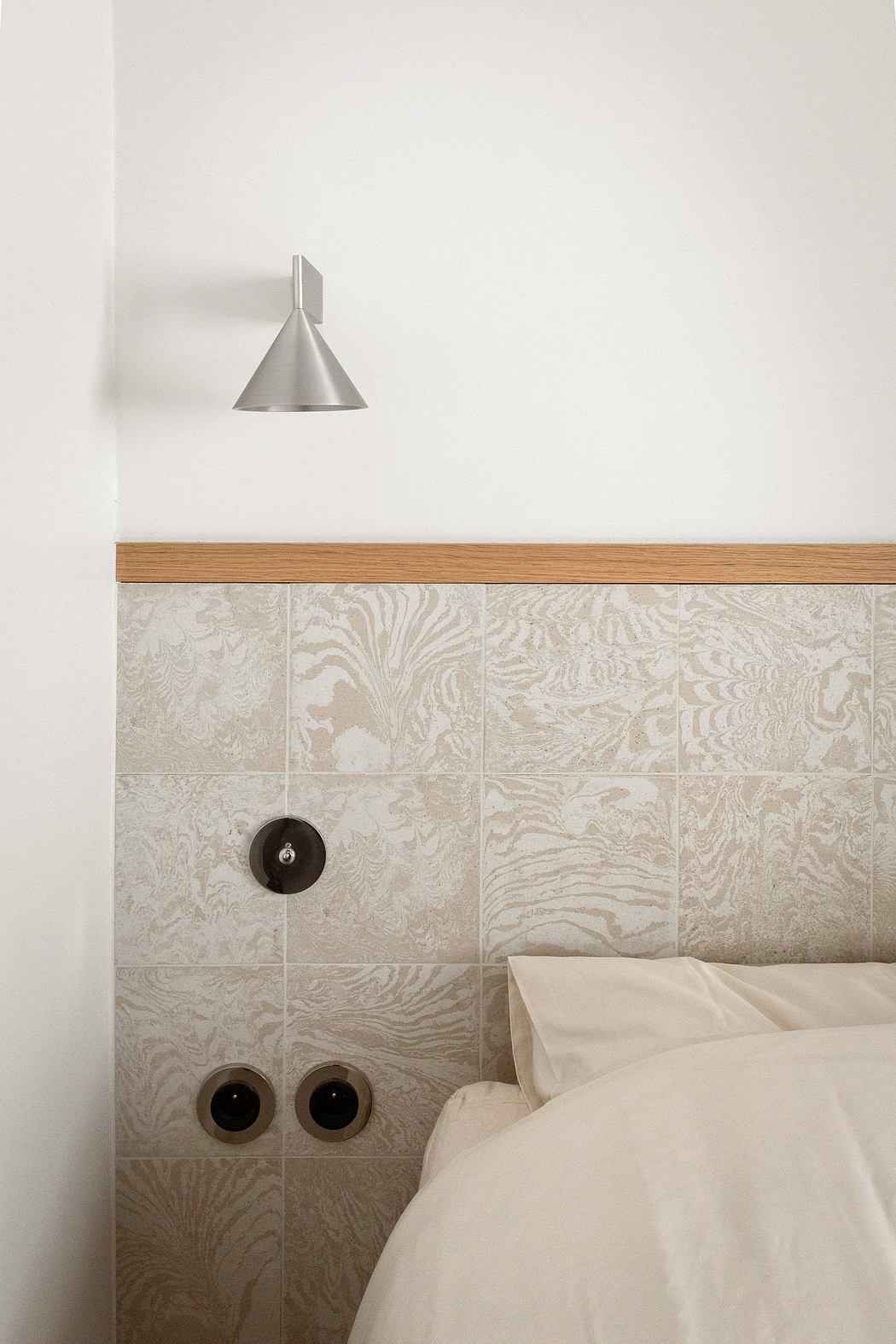 A minimalist bedroom design with patterned tile walls, a wooden ledge, and a modern light fixture.