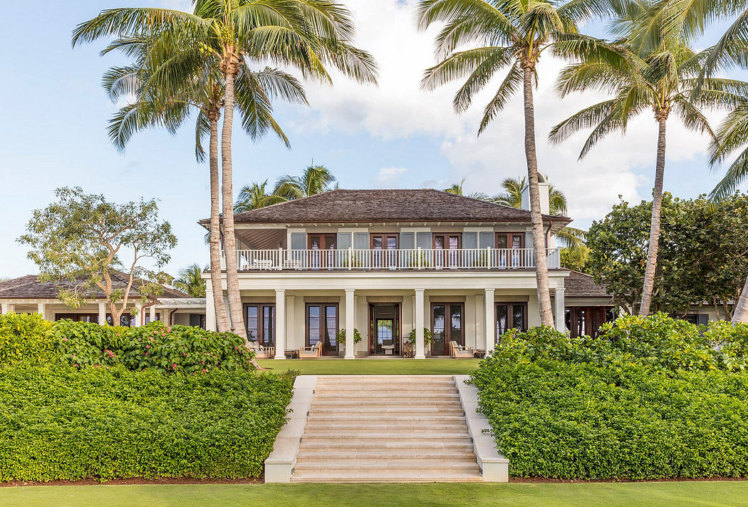 A grand, two-story tropical estate with lush palm trees, a covered porch, and symmetrical design.