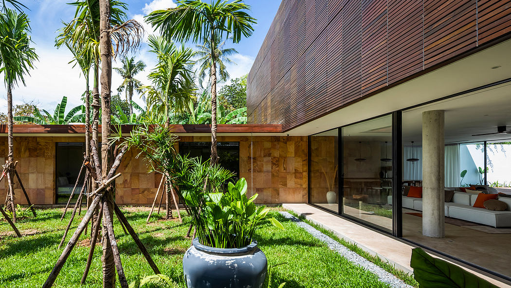 Modern tropical villa with lush greenery, stone walls, and glass panels blending indoor and outdoor spaces.