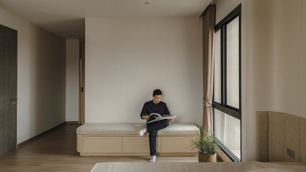 Minimalist bedroom design with built-in bench seating, large window, and a person reading a book.
