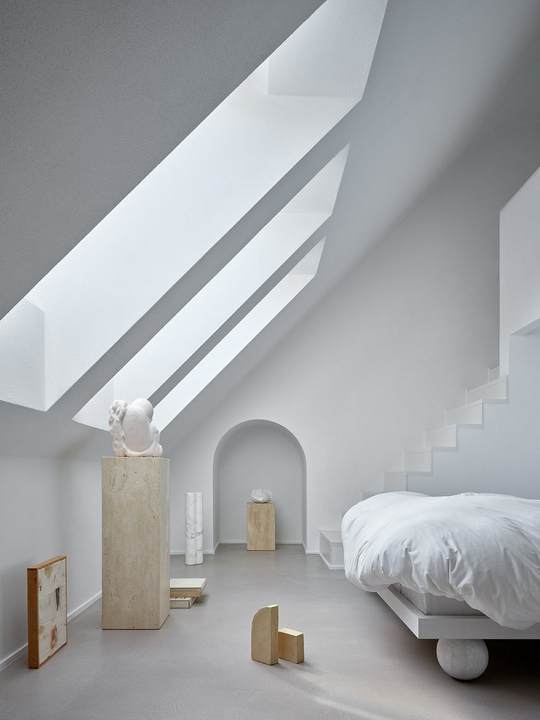 Minimalist bedroom with white walls, angled ceilings, and sculptural wooden elements.